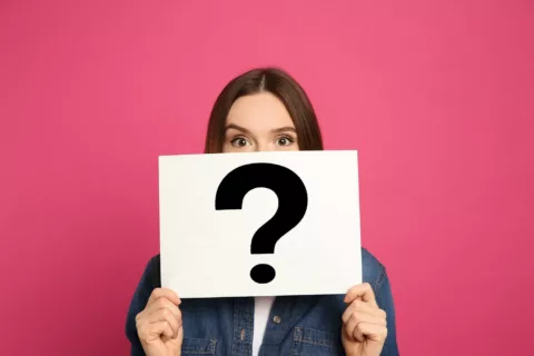 Female with a question mark in front of her face asking what is ppc, set against a pink background