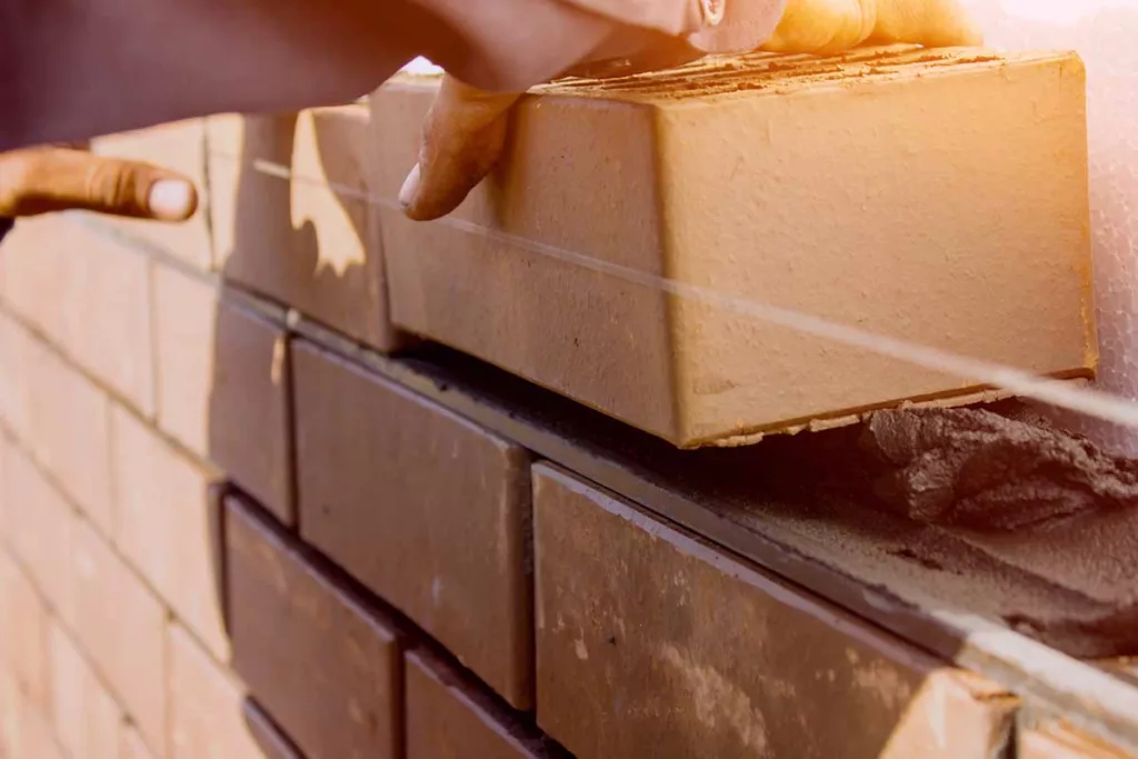 A builders hand laying a brick whilst building a wall
