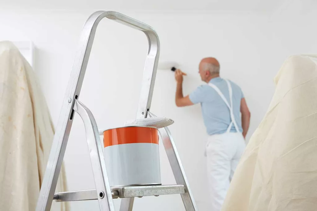 a decorator decorating a room with a paint tin on a ladder