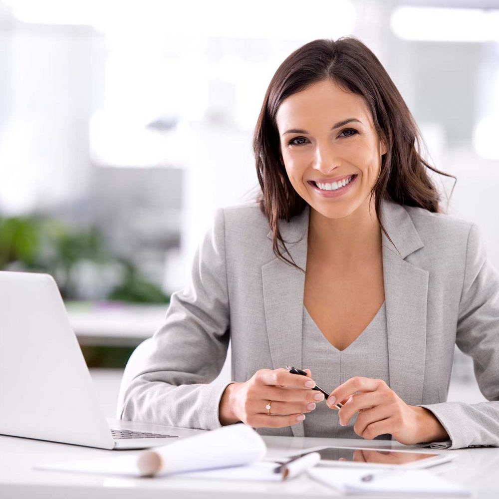 Business woman smiling sat at a desk with a laptop